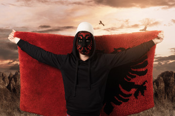 Wall Mural - young man with painted albanian flag on face standing in front of rocky landscape and flying the fluffy albanian flag