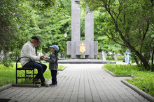 Grandpa Is Walking With Her Grandson In A Spring Park. Grandson And Grandfather On A Walk. Grandpa Is Talking To A Little Boy.