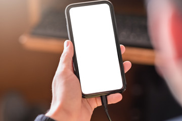 Poster - Man hand holding smartphone and use device and charging device while using with blank white screen for mockup