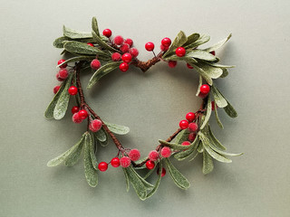 decorative mistletoe wreath with frosted leaves and red berries shaped as a heart. flat lay, top vie