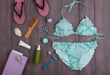 Sea Holidays / Travel Concept - Blue Beautiful Swimsuit, Flip Flops And Accessories: Wooden Hairbrush, Sunscreen, Bottles With Cream, Razor And Seashells