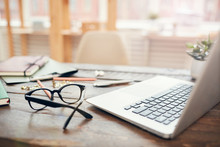Background Image Of Business Office With Laptop And Supplies On Wooden Desk, Focus On Black Hard Rim Glasses In Foreground, Copy Space