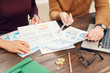 © Seventyfour - Cropped portrait of two young business people or college students pointing at data charts and sitting at wooden desk while working or studying