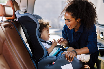 happy mother looking at her son in a baby seat. young female preparing kid for a trip.