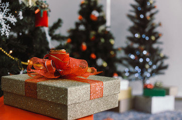 Wall Mural - gift box with red ribbon on desk with christmas tree and bokeh light background, new year gift, holiday family celebration, happy new year and merry christmas festival concept, vintage tone effect.