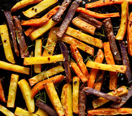 French fries,  baked fries from different types and colors of potatoes sprinkled with herbs and spices on a black background, top view