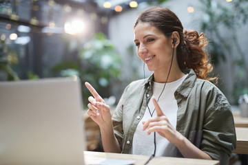 Wall Mural - Portrait of modern young woman listening to music and dancing while using laptop on outdoor terrace in cafe, copy space