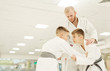 © AnnaStills - Two boys in kimono practicing technique with their coach standing near by and teaching them during training in gym