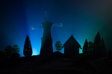 Windmill Silhouette Standing On Hill Against The Night Sky. Night Decor With Old Windmill On Hill With Horror Toned Foggy Background With Light.