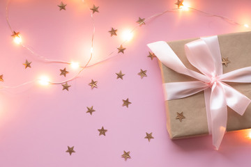 Gift in craft paper with a pink bow on a pink background with holographic sparkles in the form of stars. Template  banner for greeting card your text design 2020. New year, christmas, birthday