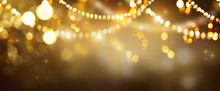 Christmas Gold Glowing Background. Golden Holiday Abstract Glitter Defocused Backdrop With Blinking Stars And Garlands. Tinsel Blurred Gold Bokeh On Black Background. Festive Defocused Elegant Border