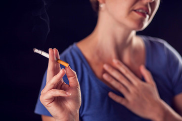 Woman smokes cigarette and has lungs or heart pain on black background. Nicotine addiction and health problem concept