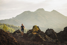 Young Athlete Man Trail Running In Mountains In The Morning. Amazing Volcanic Landscape Of Bali Mount Batur On Background. Healthy Lifestyle Concept.