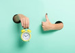 Female hand hold alarm clock and show tumb sign through a hole on neon mint background. Just in time concept.