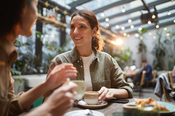 portrait of beautiful young woman talking to friend while enjoying evening on outdoor terrace in caf