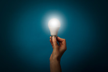 Female Hand Holds A Working LED Lamp On A Blue Background. Energy Saving Concept, Alternative Energy Sources, Idea