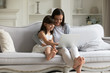 Daughter and mother seated on couch having fun using laptop