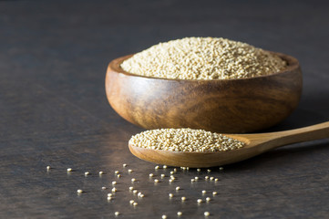 White quinoa seeds in wooden spoon and bowl on rustic background ( Chenopodium quinoa ), cereal healthy vegetarian food gluten free to lose weight