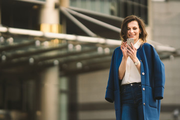 Office buildings city people in suit. Caucasian businesswoman using smartphone with hand. Business concept. Portrait stylish business woman in fashionable clothes holding Phone near office building