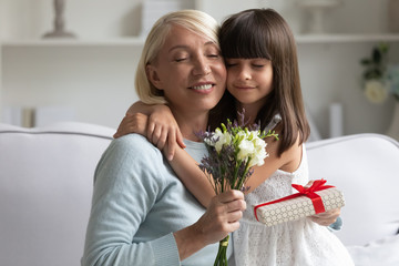 Loving granddaughter cuddles grandmother congratulating her with anniversary