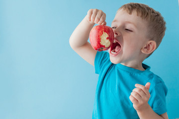 Wall Mural - Baby child holding and eating red apple on blue background, food, diet and healthy eating concept