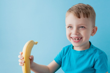 Wall Mural - Little Boy Holding and eating an Banana on blue background, food, diet and healthy eating concept