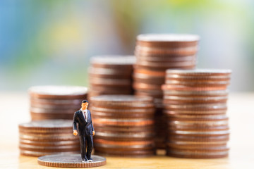 Poster - Miniature businessman standing on coin with money stack coin background. Business finance growth concept.