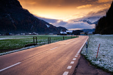 Road At Sunset Leading To Snow Covered Mountain Peaks