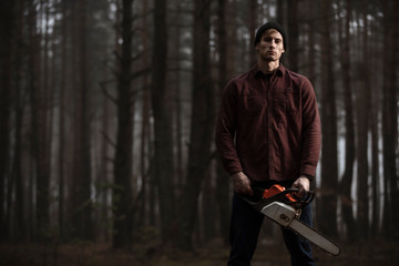 Lumberman working with chainsaw in the forest. Strong lumberjack with the chainsow in the forest.Stylish lumberman getting ready for work. Lifestyle.