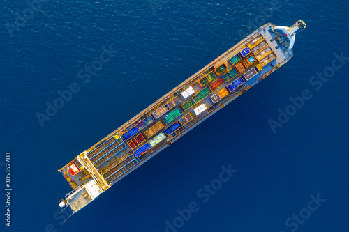 Cargo Ship loaded with colourful Containers and large crates cruising at sea, Top down aerial view.