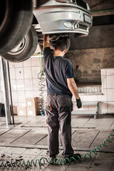 Wall Mural - Car mechanic working in a repair garage with hydraulic car lift