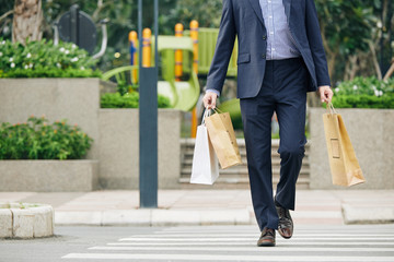 Cropped image of man holding many paper-bags when walking in city and crossing road