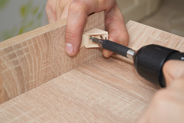 A man is busy assembling furniture and screwing a plastic furniture corner with a screwdriver