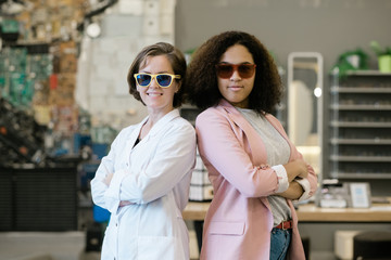 Canvas Print - Two young multicultural females in sunglasses standing close to each other