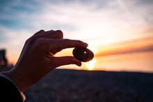 Person Holds A Stone With A Hole At Sunset. Find A Amulet And Make A Wish