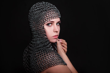 Wall Mural - Portrait of a beautiful, young girl in a chainmail hood on a black background. Model with clean skin.