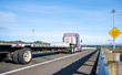 © vit - Big rig brown semi truck with empty step down semi trailer running on the straight highway with traffic sign