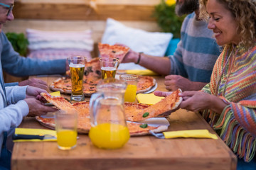 close up of hands with glass with beer and orange juice clinking together at the centre of the table - two big pizzas on the wooden table