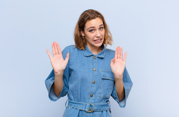 Wall Mural - young blonde woman looking nervous, anxious and concerned, saying not my fault or I didn‚Äôt do it against flat color wall