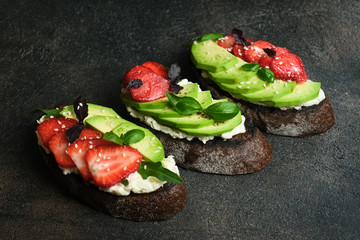 Wall Mural - Toast or sandwich with avocado, cheese, strawberries, herbs and seeds on a dark background. An idea for bruschetta or for a healthy snack. Healthy vegan breakfast.