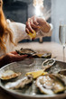 Oysters in a round metal plate with ice, lemon. Female’s hand pours open lemon on oysters. Seafood restaurant