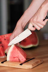 Hands chop watermelon with a knife on a bamboo cutting board