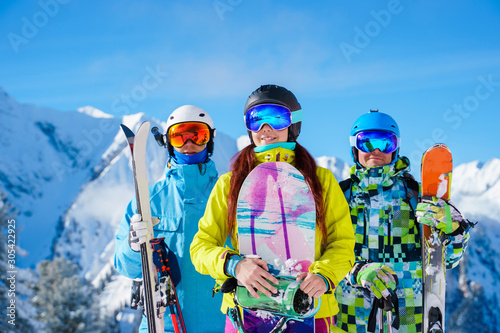Fotomural Two men and woman with snowboard and skis standing on snow resort against backdrop of mountain