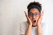Close up of young african american girl with glasses making funny face with mouth open by white wall