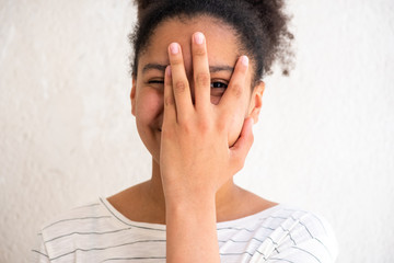 cheerful young african american girl with hand covering face by white background