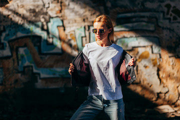 Wall Mural - Girl wearing t-shirt, glasses and leather jacket posing against street , urban clothing style. Street photography