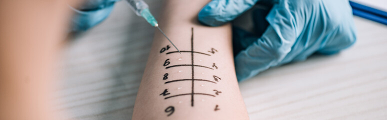 panoramic shot of allergist in latex gloves holding syringe near woman while doing allergy test in clinic