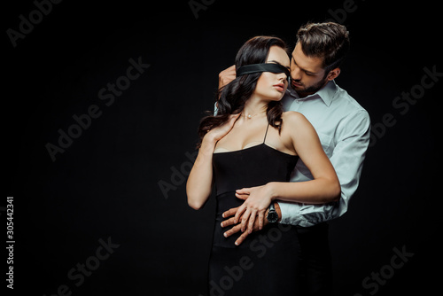 Fotomural handsome bearded man looking at blindfolded girlfriend isolated on black