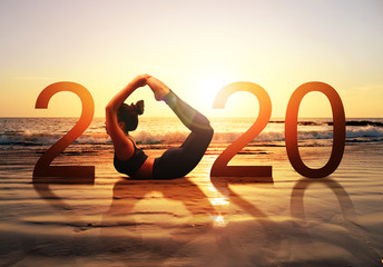 Wall Mural - Happy new year card 2020. Silhouette of healthy girl doing Yoga Bow pose on tropical beach with sunset sky background, woman practicing yoga as a part of the Number 2020 sign.