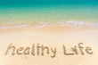 Healthy life, lettering on golden sand  beach with wave and clear blue sea. Message handwritten in sand on beautiful beach. Healthy life sign on holiday vacation concept for background and copy space.